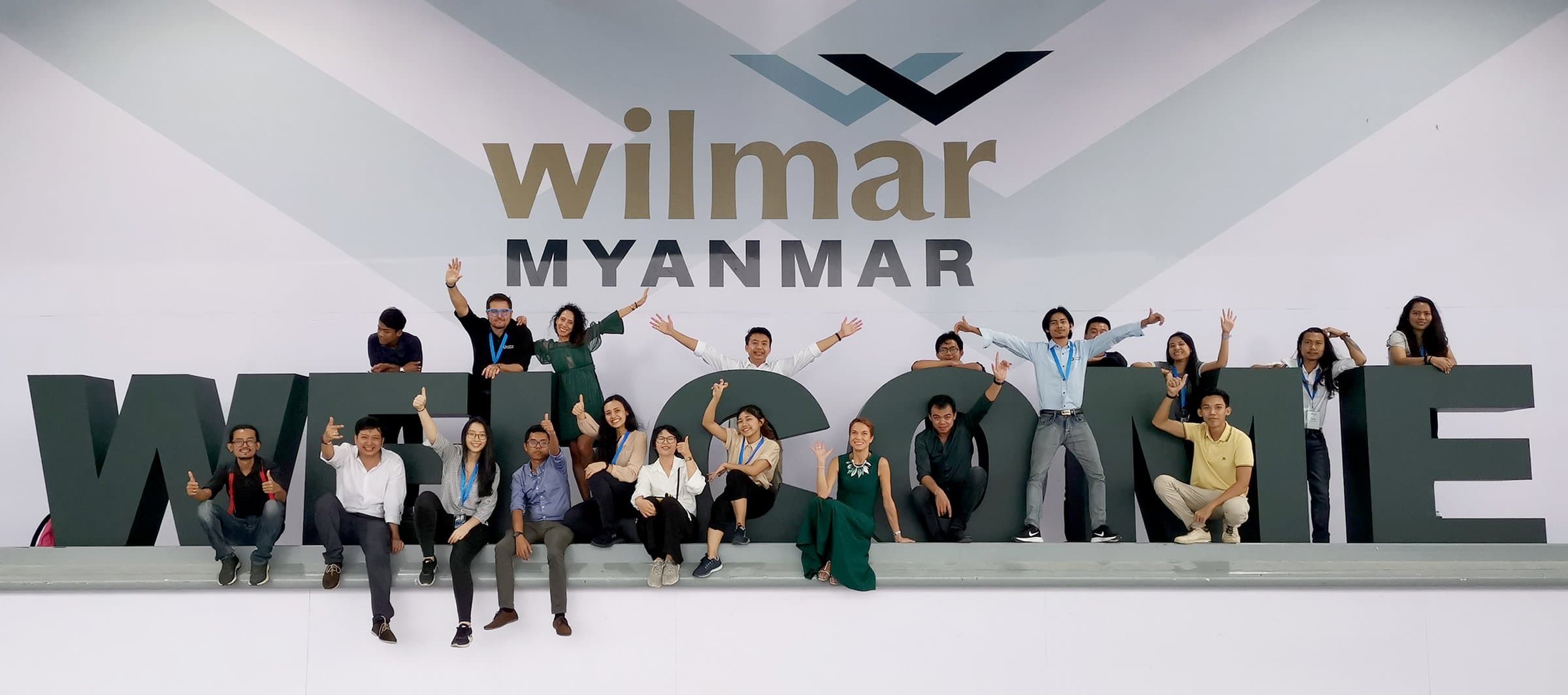 The team on the WELCOME letters under the Wilmar Myanmar backdrop